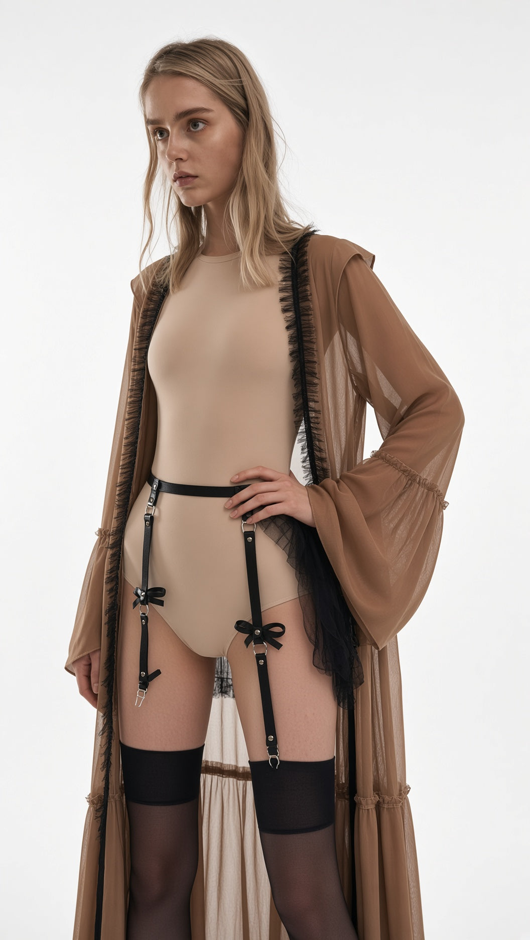 A model wearing a beige bodysuit with black garter straps and thigh-high stockings, styled with a sheer brown fringed robe over a plain white studio background.