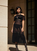 Woman wearing a black lace outfit standing against a stone wall.