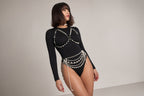 A woman modeling a black long-sleeve bodysuit with decorative white pearl-like embellishments across the chest and waist, photographed against a plain light gray studio background.