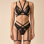 A model wearing a black lace and strappy lingerie set against a solid beige background.