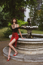 Woman in a black top and red skirt standing by a fountain in a garden.